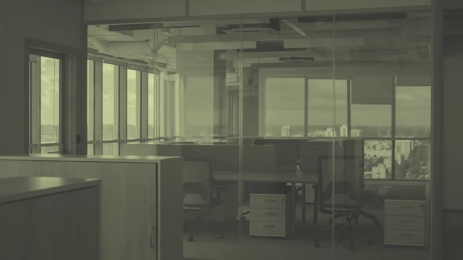 An empty open-plan office with unused desks and chairs behind a glass wall